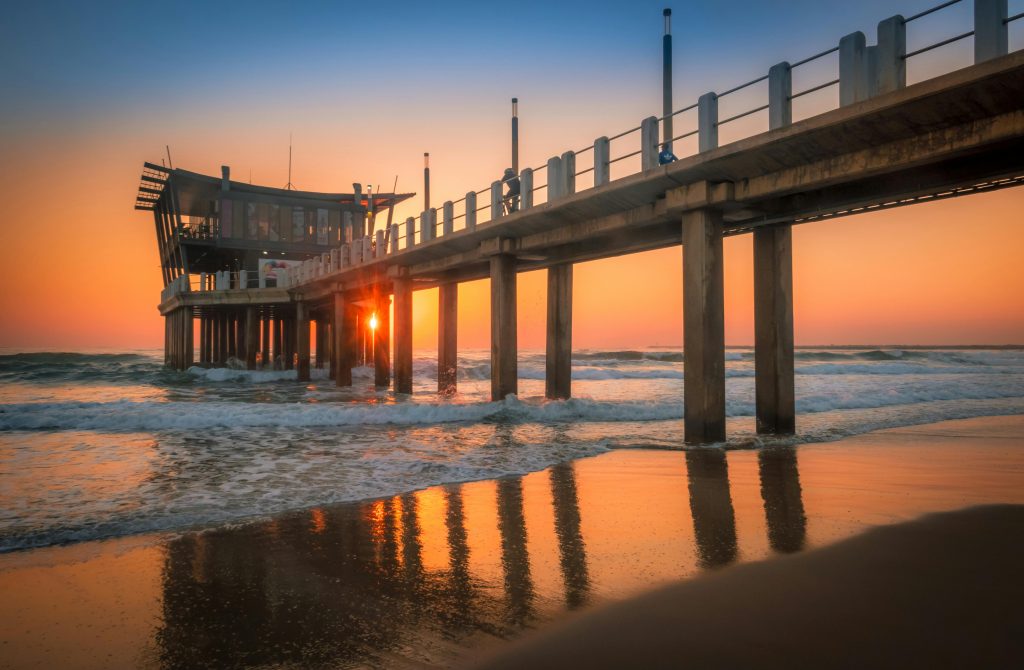 Beautiful sunrise at the Durban pier with waves gently lapping the shore in a serene coastal scene.